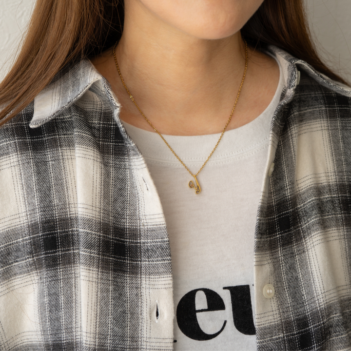 女性が白いTシャツとチェックのシャツを着て、金色のY字ネックレスを着用