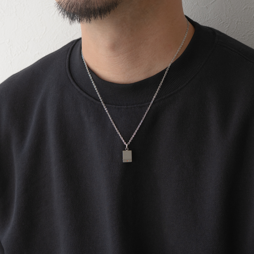 男性が黒いスウェットシャツを着て、シルバーのチェーンネックレスと長方形のペンダントを着用