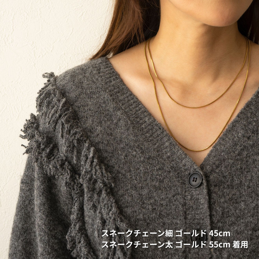 女性がグレーのカーディガンを着て、2本のゴールドのスネークチェーンネックレスを重ね付けしている