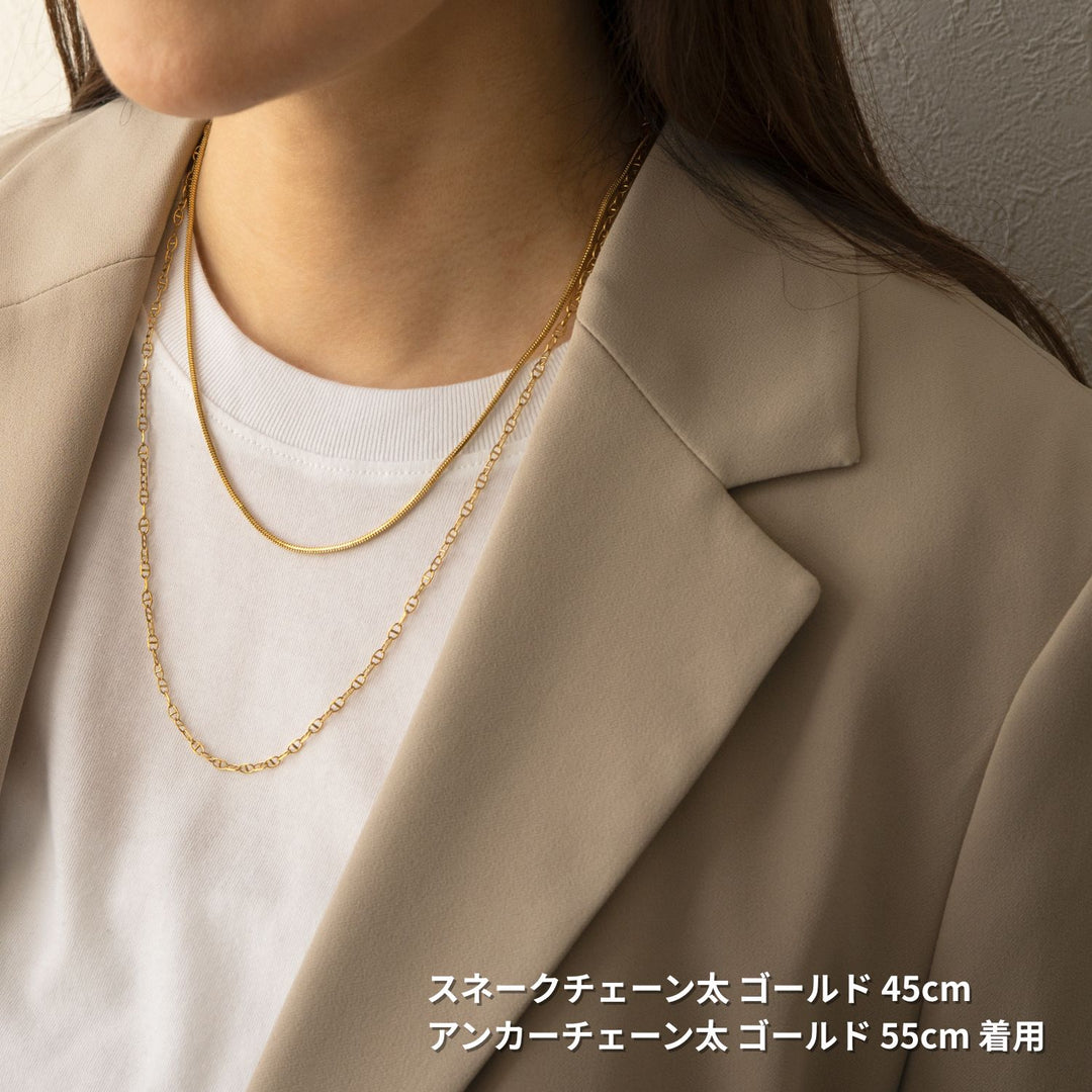 ベージュのブレザーと白いTシャツを着た女性が、2本のゴールドネックレスを重ね付けしている