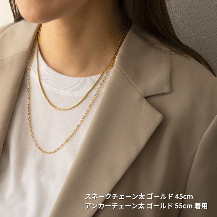 ベージュのブレザーと白いTシャツを着た女性が、2本のゴールドネックレスを重ね付けしている