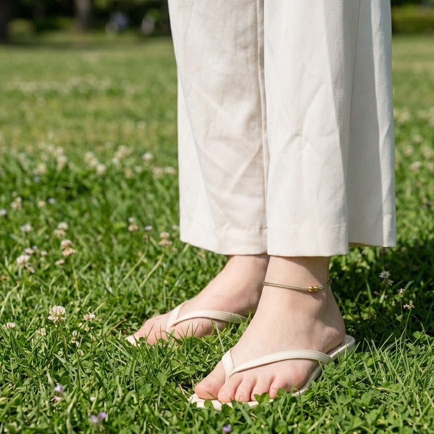 女性が白いサンダルと足首にアンクレットを付けて草の上に立っている