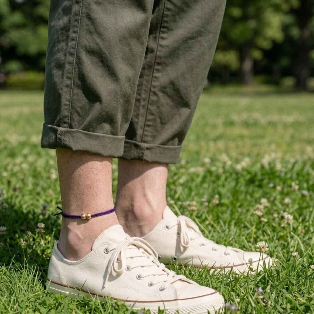 男性がカーキ色のパンツと白いスニーカーを履き、足首に紫色のアンクレットを着けている